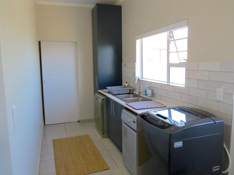 A functional laundry room featuring built-in cabinetry, a stainless steel sink, subway tile backsplash, and tiled flooring with natural light from a window.