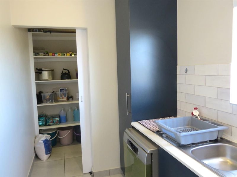 A functional scullery featuring built-in dark cabinetry, a stainless steel sink, subway tile backsplash, and an integrated walk-in pantry with shelving.