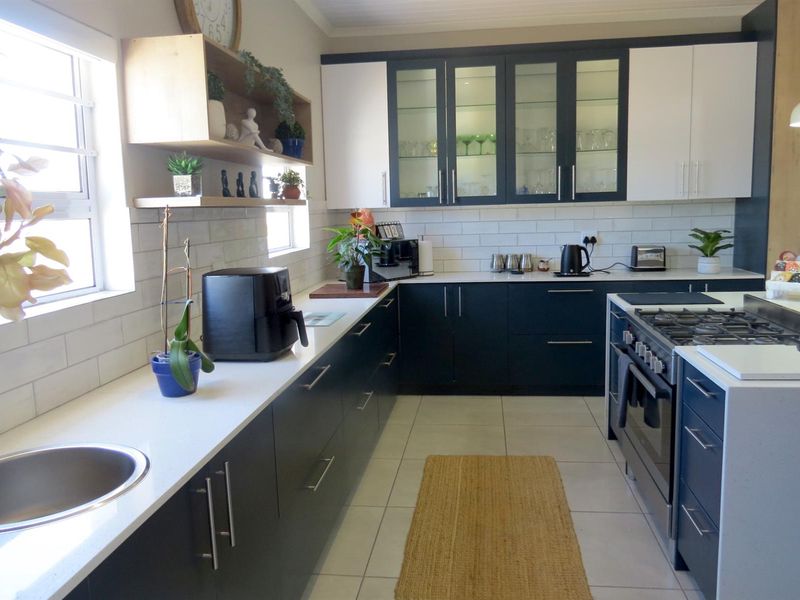 Modern kitchen featuring dark cabinetry, white quartz countertops, subway tile backsplash, gas stove, and glass-front display cabinets.
