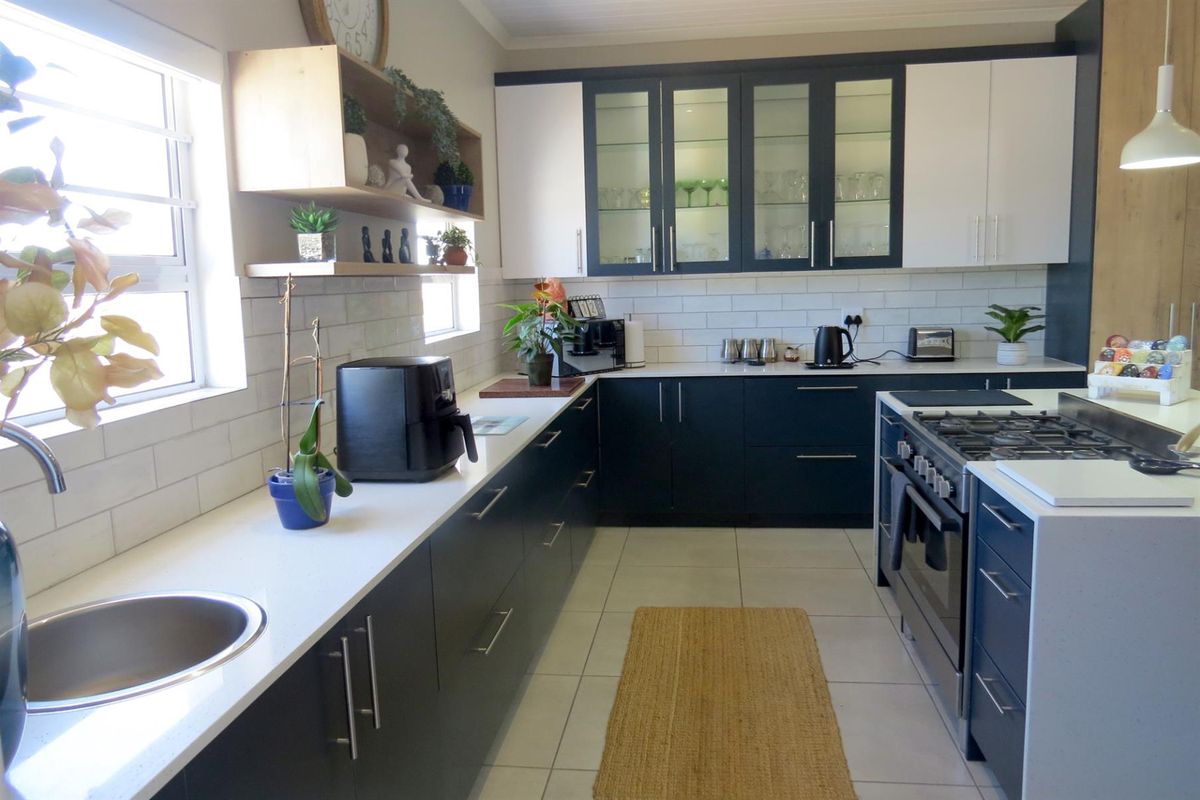 Modern kitchen featuring dark cabinetry, white quartz countertops, subway tile backsplash, gas stove, and glass-front display cabinets.