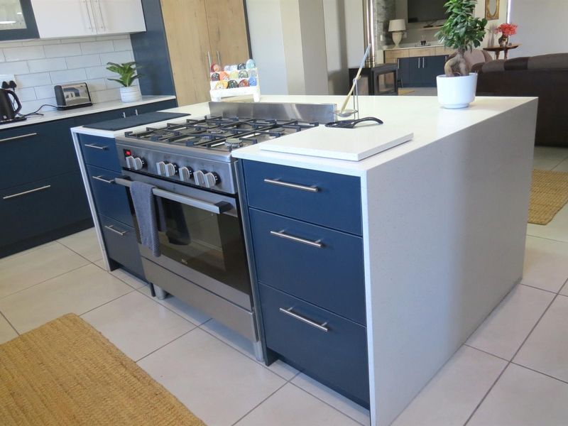 Modern kitchen featuring a central island with a gas cooktop, built-in oven, and sleek blue cabinetry with light-colored quartz countertops.