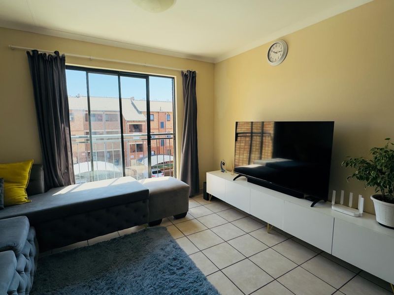 A living room featuring tiled flooring and a sliding glass door providing access to a balcony with an urban view.