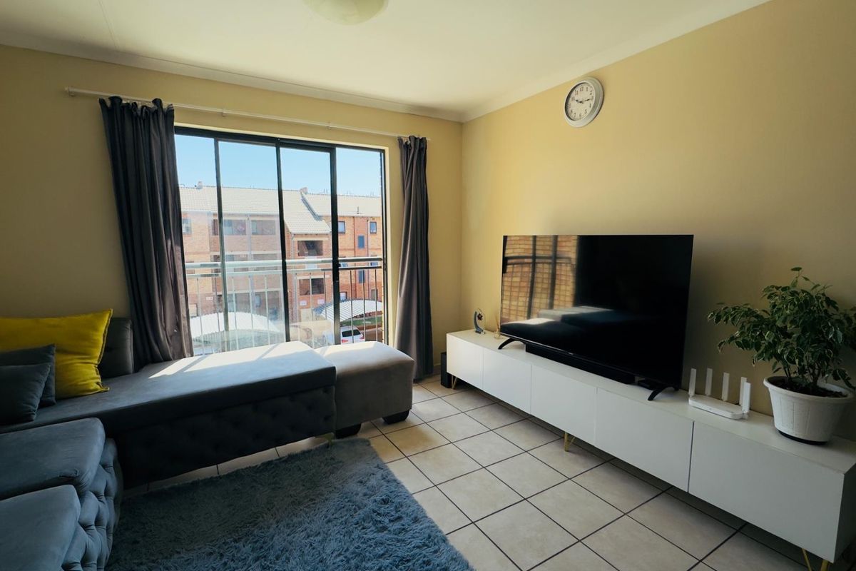 A living room featuring tiled flooring and a sliding glass door providing access to a balcony with an urban view.