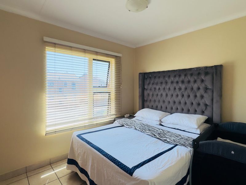 A functional bedroom featuring tiled flooring, a built-in wardrobe, and a window fitted with venetian blinds, providing natural light.