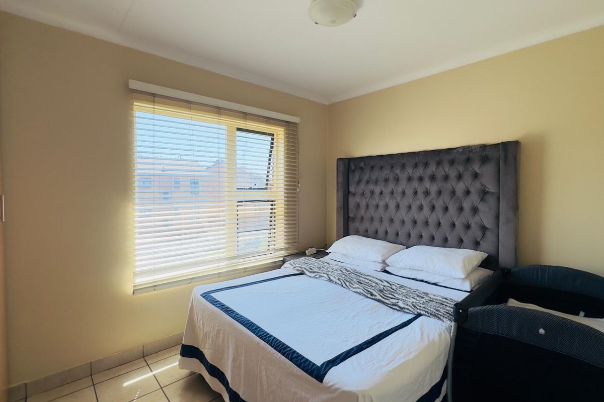 A functional bedroom featuring tiled flooring, a built-in wardrobe, and a window fitted with venetian blinds, providing natural light.
