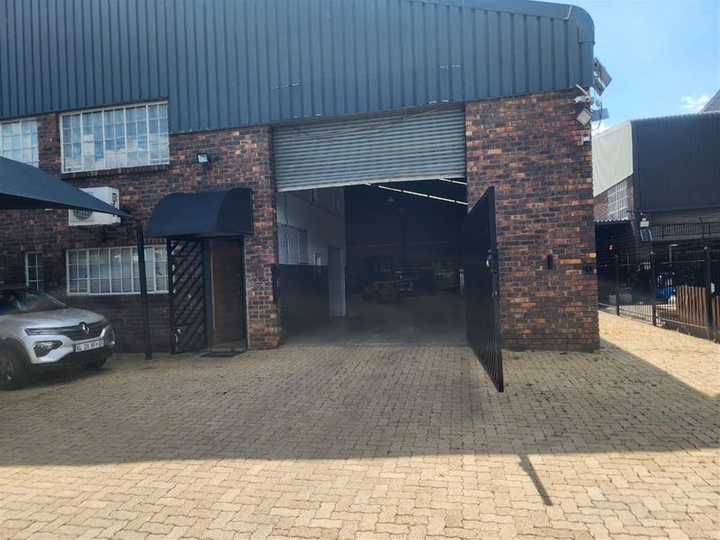 Commercial warehouse unit featuring a brick facade, roller shutter door access, and paved exterior parking area.