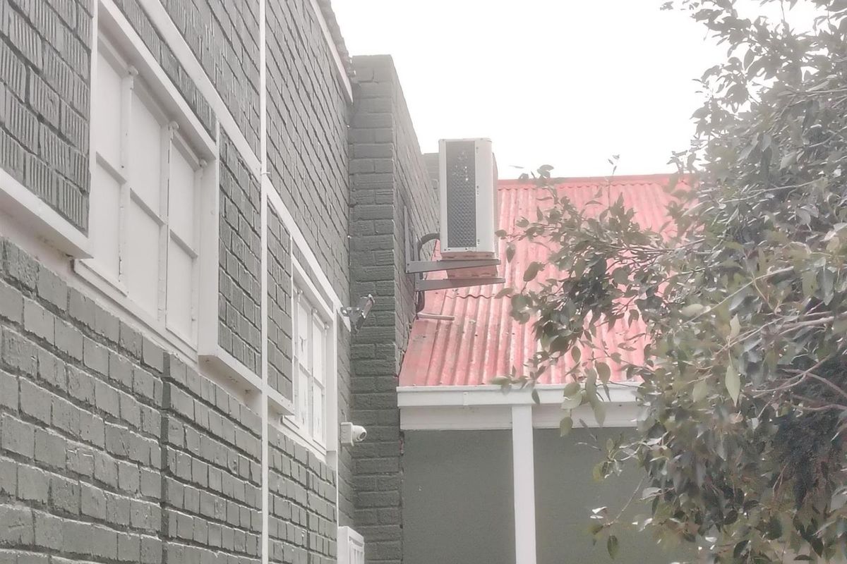 Exterior view of the building facade featuring painted brickwork, a corrugated metal roof, and a wall-mounted air conditioning unit.