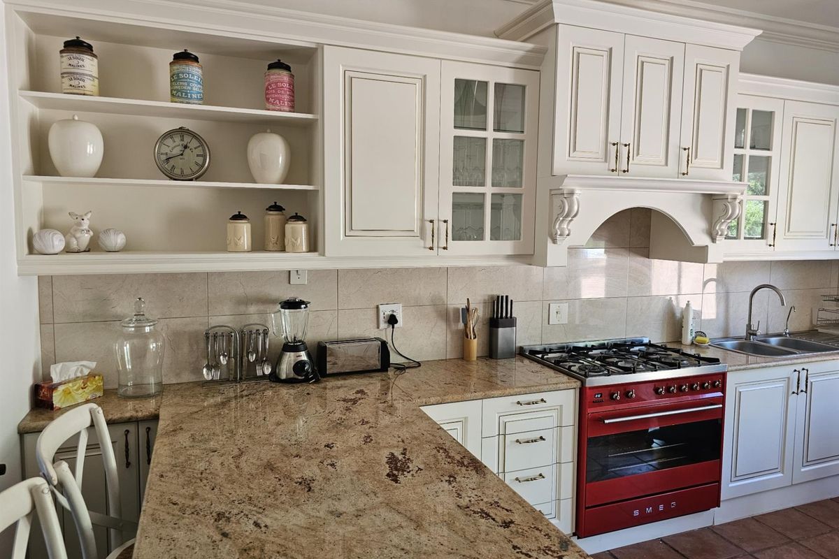 A well-appointed kitchen featuring cream cabinetry, granite countertops, a tiled backsplash, and a prominent red Smeg freestanding oven and gas hob.