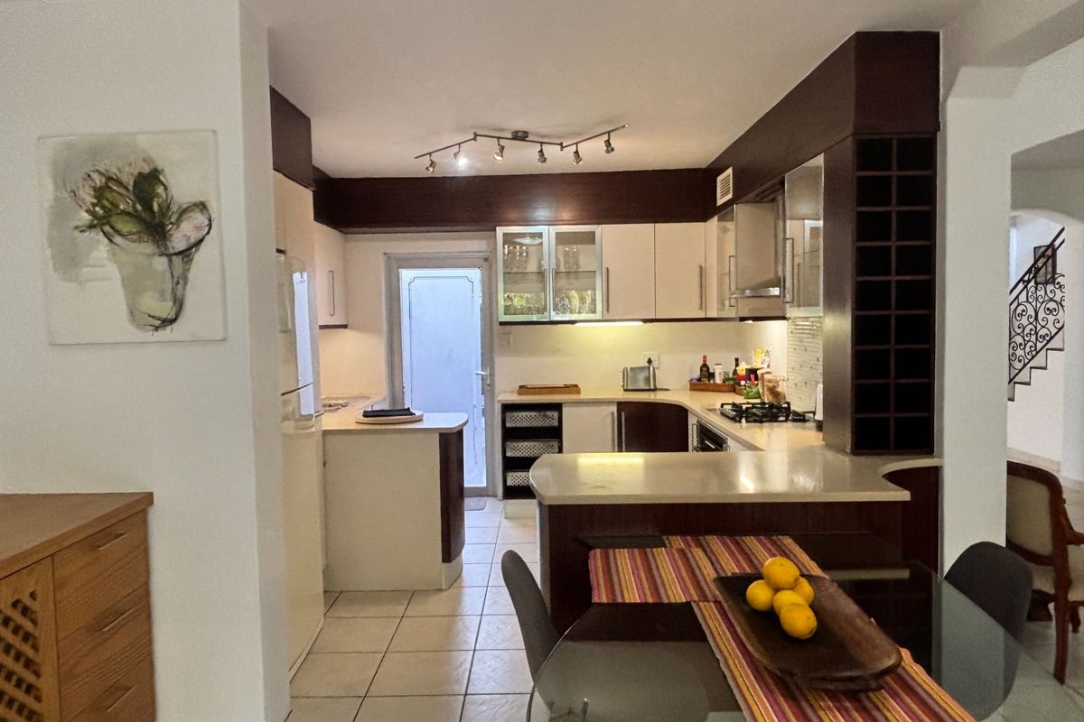 A functional kitchen featuring dark wood cabinetry, stone countertops, a built-in gas hob, and tiled flooring, with an adjacent breakfast bar area.