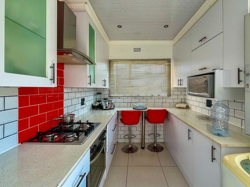 Compact galley kitchen featuring white cabinetry, stone-look countertops, a gas hob, built-in oven, and a breakfast nook with subway tile backsplash.
