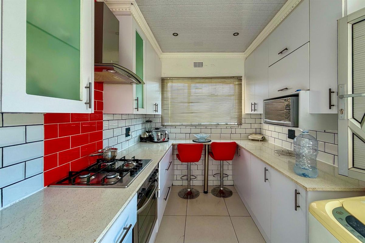 Compact galley kitchen featuring white cabinetry, stone-look countertops, a gas hob, built-in oven, and a breakfast nook with subway tile backsplash.