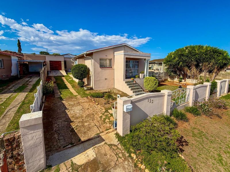 Front exterior view of a single-story house featuring a paved driveway, gated entrance, and established garden area.