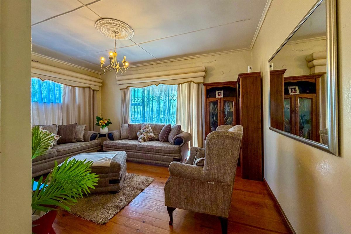 A traditional living room featuring original timber flooring, decorative ceiling rose, and large windows with security bars.