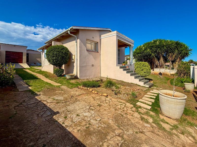 A view of the property's side and rear exterior, featuring a paved driveway, landscaped garden area, and concrete steps leading to the entrance.