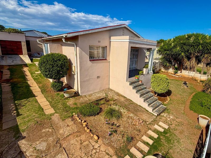 A detached single-story house featuring a covered front porch, tiled entrance steps, and a surrounding garden with paved pathways and a driveway.