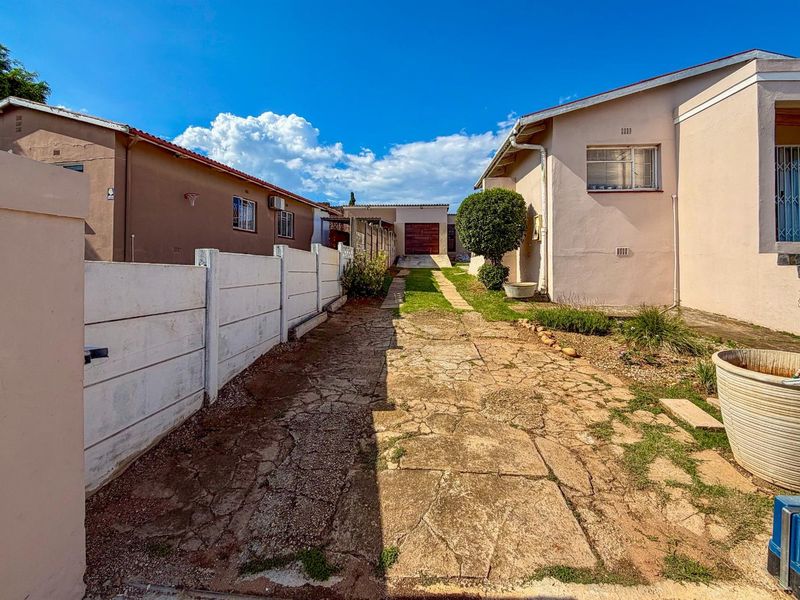 A view of the side driveway and exterior path leading towards the rear garage, featuring concrete boundary walls and paved walkway.