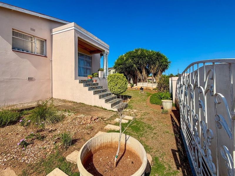 Exterior view of the house featuring a covered entrance porch with steps, a side garden area, and decorative metal boundary fencing.