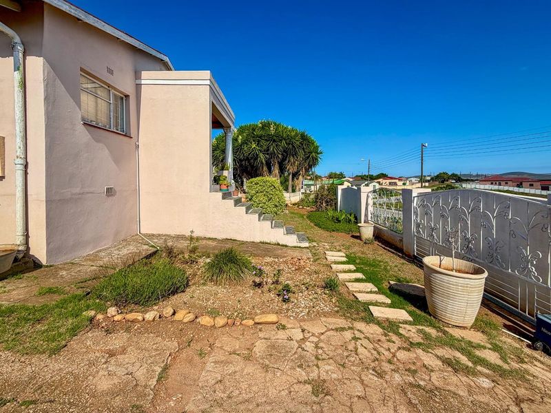A view of the side exterior of the house featuring a concrete staircase, paved walkway, and decorative metal gate.