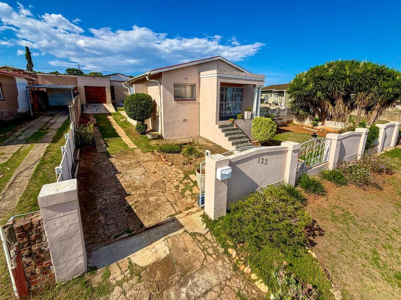 A detached single-story house featuring a front porch, paved driveway, and enclosed garden with a perimeter boundary wall.