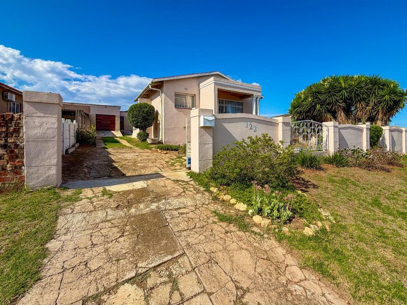 Front view of a single-story house featuring a paved driveway, perimeter boundary wall, and established garden area.