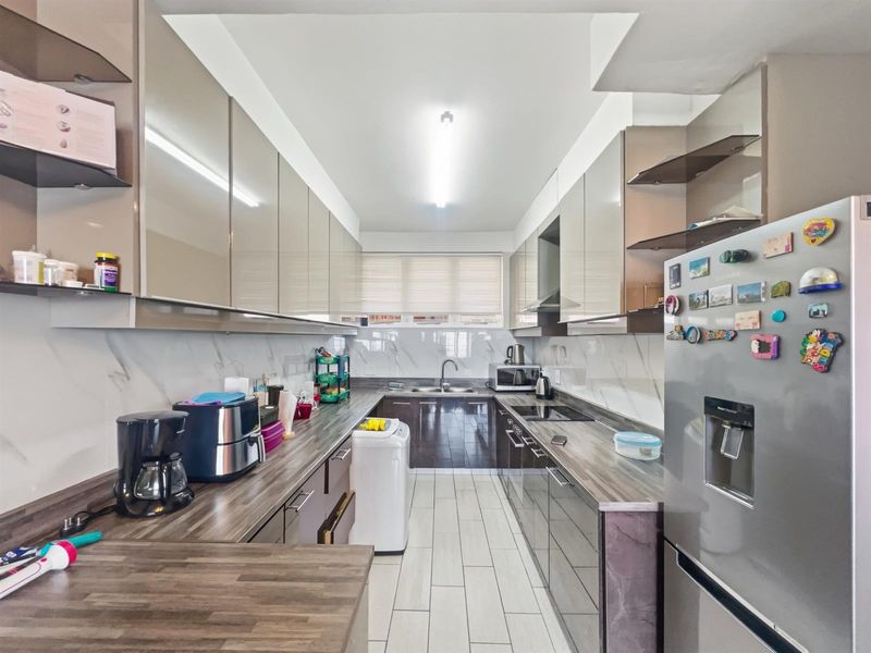 Modern galley-style kitchen featuring high-gloss cabinetry, marble-effect backsplash, wood-look laminate countertops, and integrated cooktop with extractor fan.