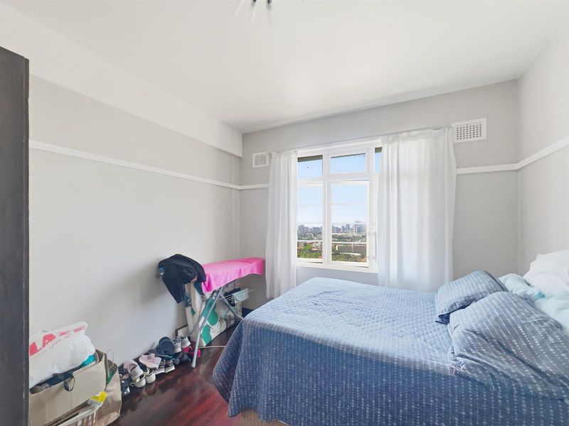 A bright bedroom featuring dark timber flooring, picture rails, and a large window offering expansive city views.