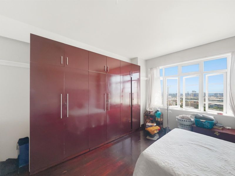 A bedroom featuring dark wood flooring and extensive built-in floor-to-ceiling cabinetry, offering ample storage space and large windows with city views.