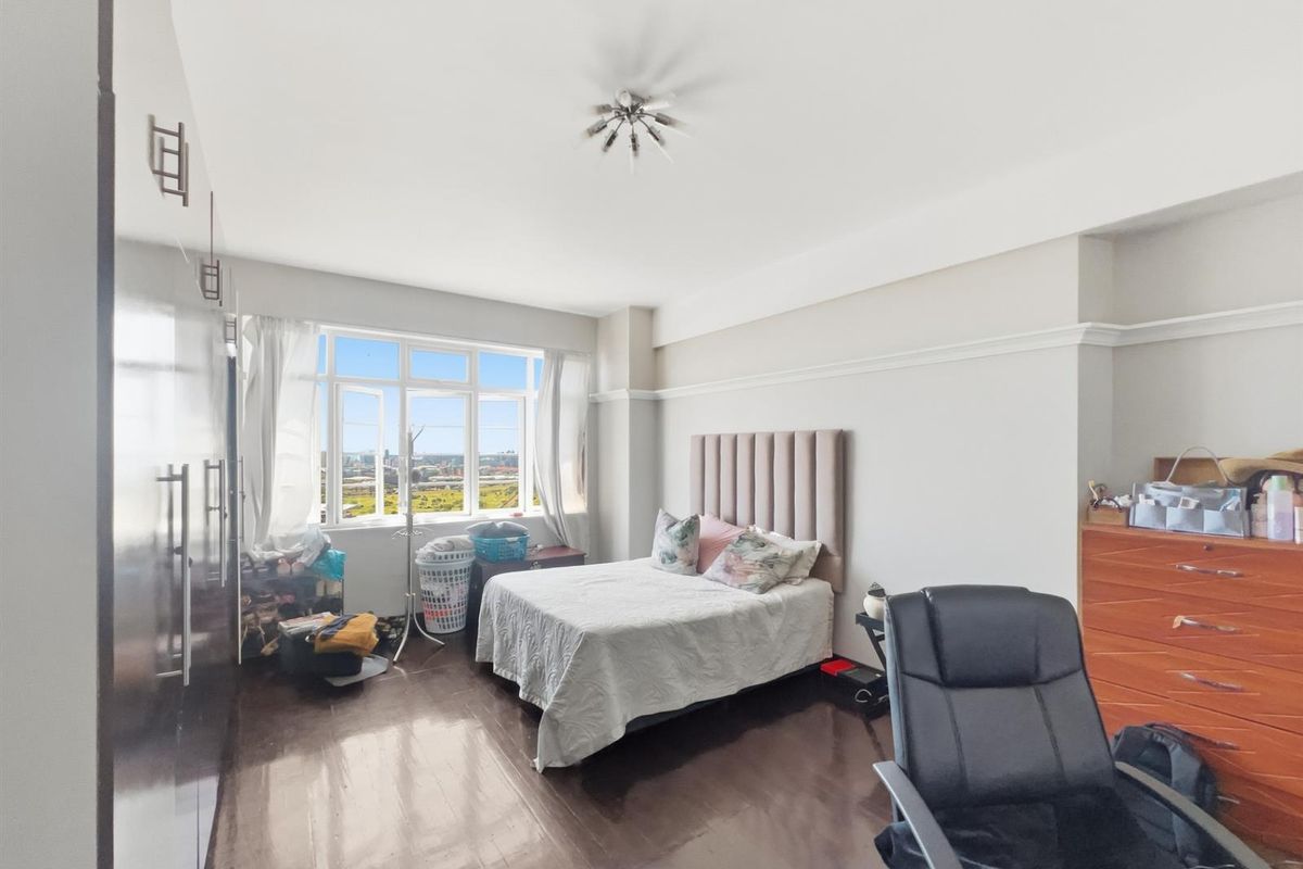 Spacious bedroom featuring dark wood-look flooring, built-in wardrobes, and large windows offering natural light and elevated views.