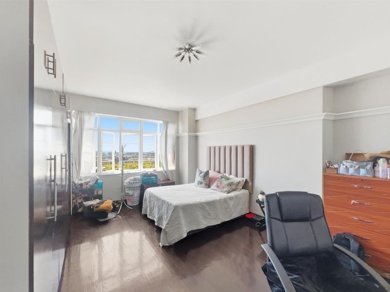 Spacious bedroom featuring dark wood-look flooring, built-in wardrobes, and large windows offering natural light and elevated views.