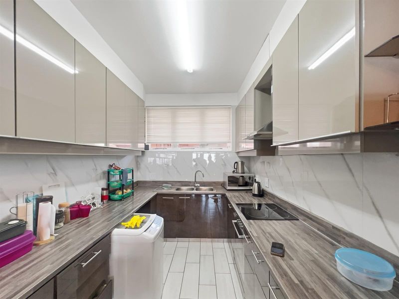 Modern galley-style kitchen featuring high-gloss cabinetry, marble-effect splashbacks, integrated cooktop, extractor fan, and double stainless steel sink with ample counter space.