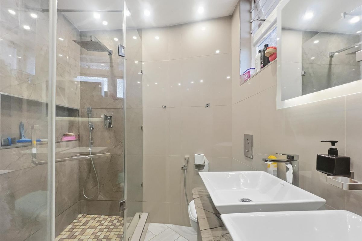Modern bathroom featuring a glass-enclosed walk-in shower, dual vessel sinks on a stone vanity, and contemporary wall tiling.