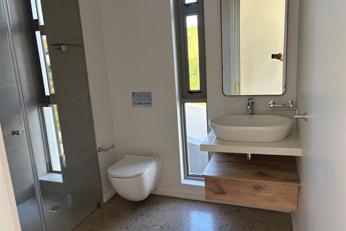 Modern bathroom featuring a wall-mounted toilet, floating vanity with vessel sink, and a glass-enclosed walk-in shower with polished concrete flooring.