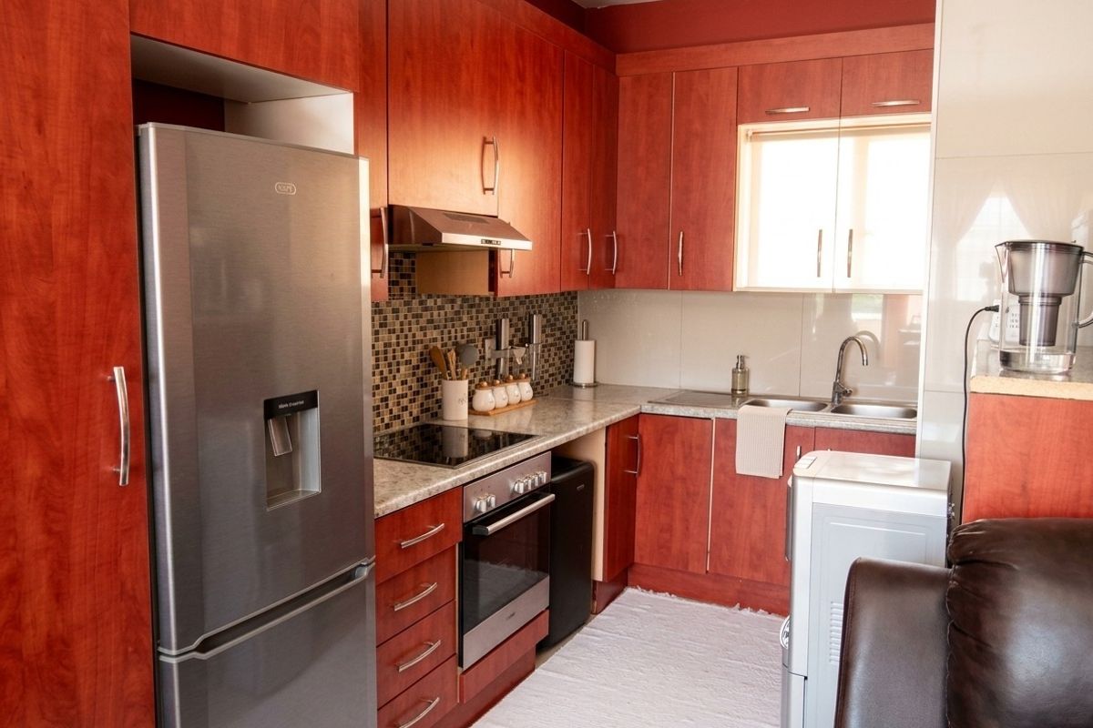 A functional kitchen featuring cherry-wood finish cabinetry, mosaic tile backsplash, laminate countertops, and integrated stainless steel appliances.