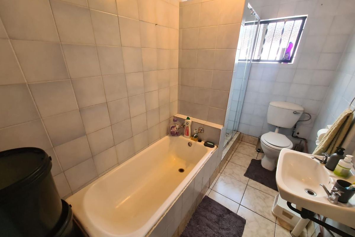 A functional bathroom featuring a built-in bathtub, separate shower enclosure, pedestal basin, and toilet with tiled walls and flooring.