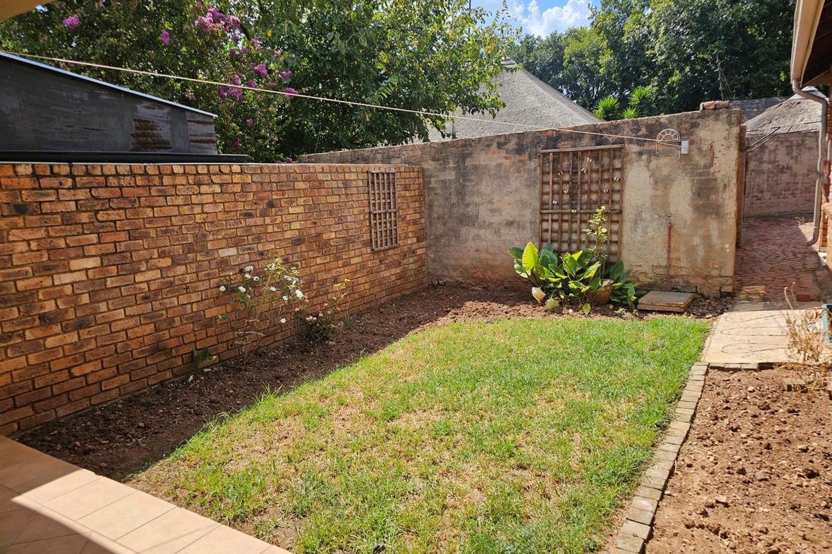A private rear garden area featuring a small lawn, tiled patio space, and brick boundary walls with trellis detailing.