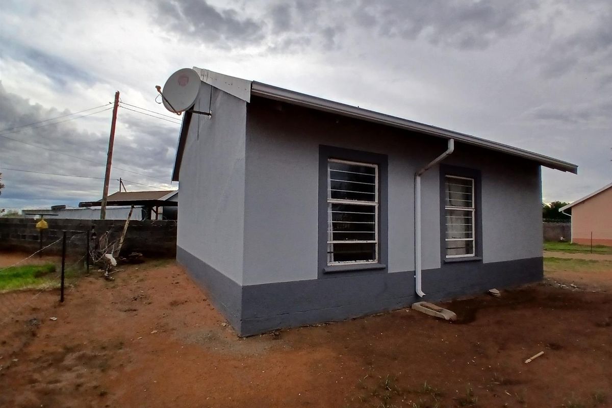 A side view of a residential house featuring a grey painted exterior, metal security bars on windows, and a satellite dish mounted on the roof.