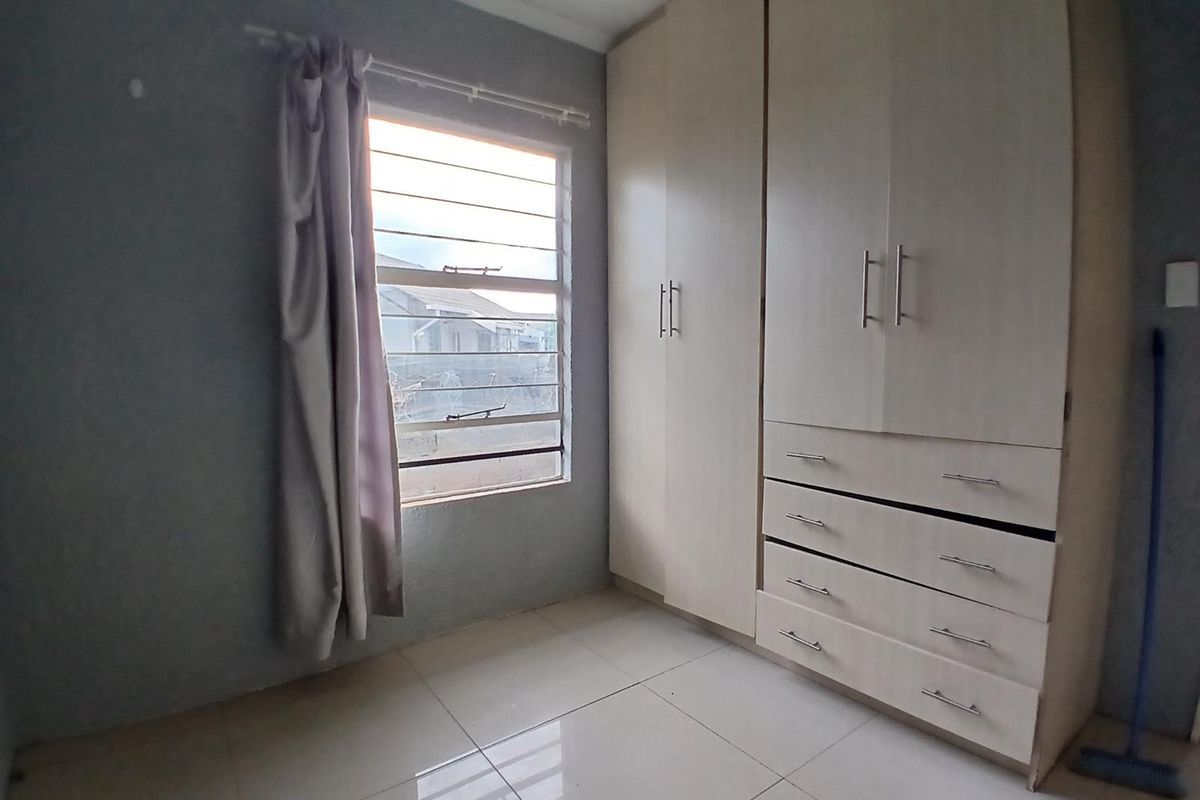 A bedroom featuring tiled flooring, a window with security bars, and built-in cabinetry with integrated drawers.