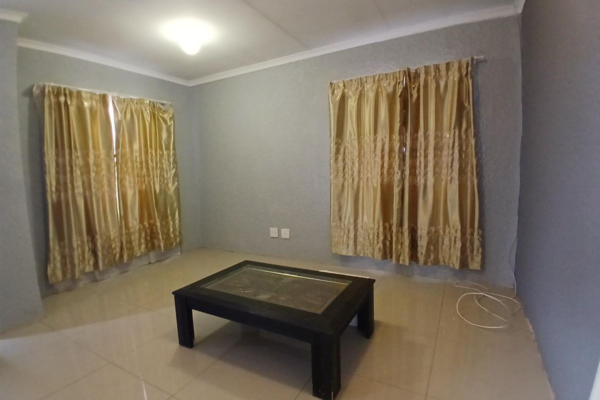 A simple living room featuring tiled flooring, grey painted walls, and dual window treatments, providing a neutral base for interior design.
