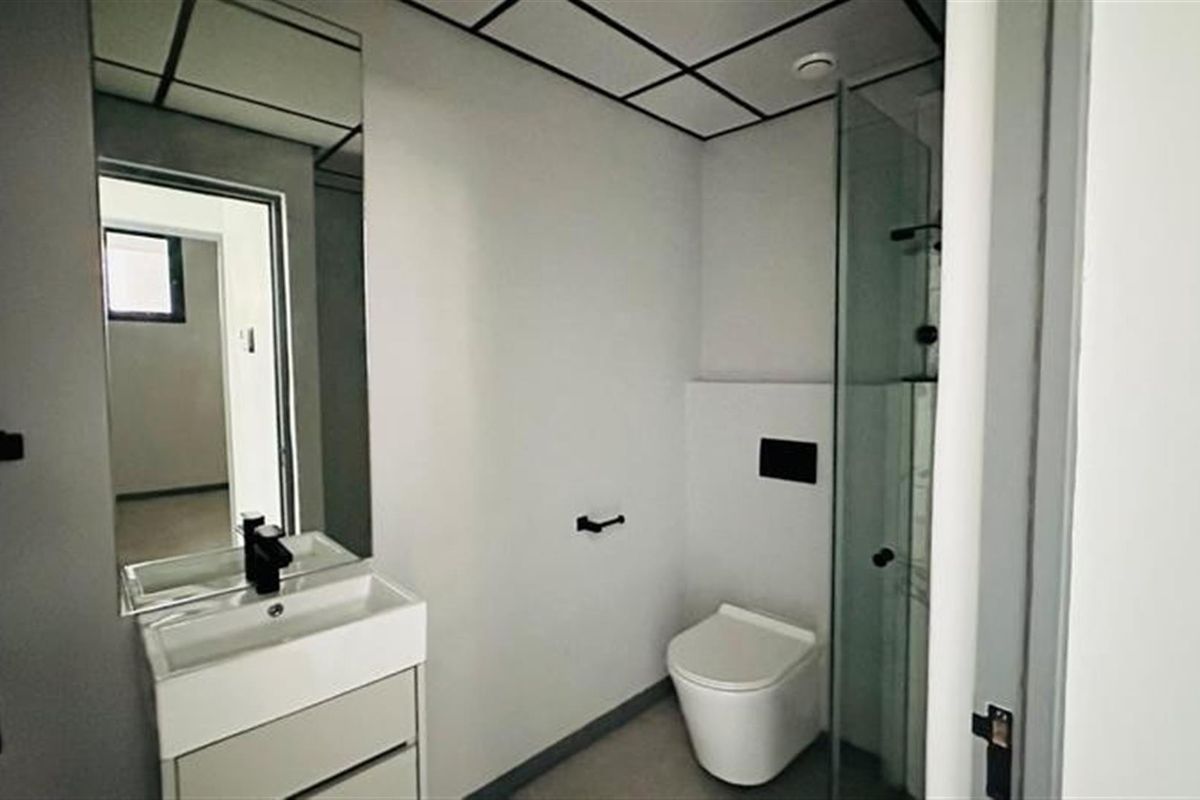 Modern bathroom featuring a wall-mounted toilet, glass-enclosed shower, and a sleek vanity with a mirror.