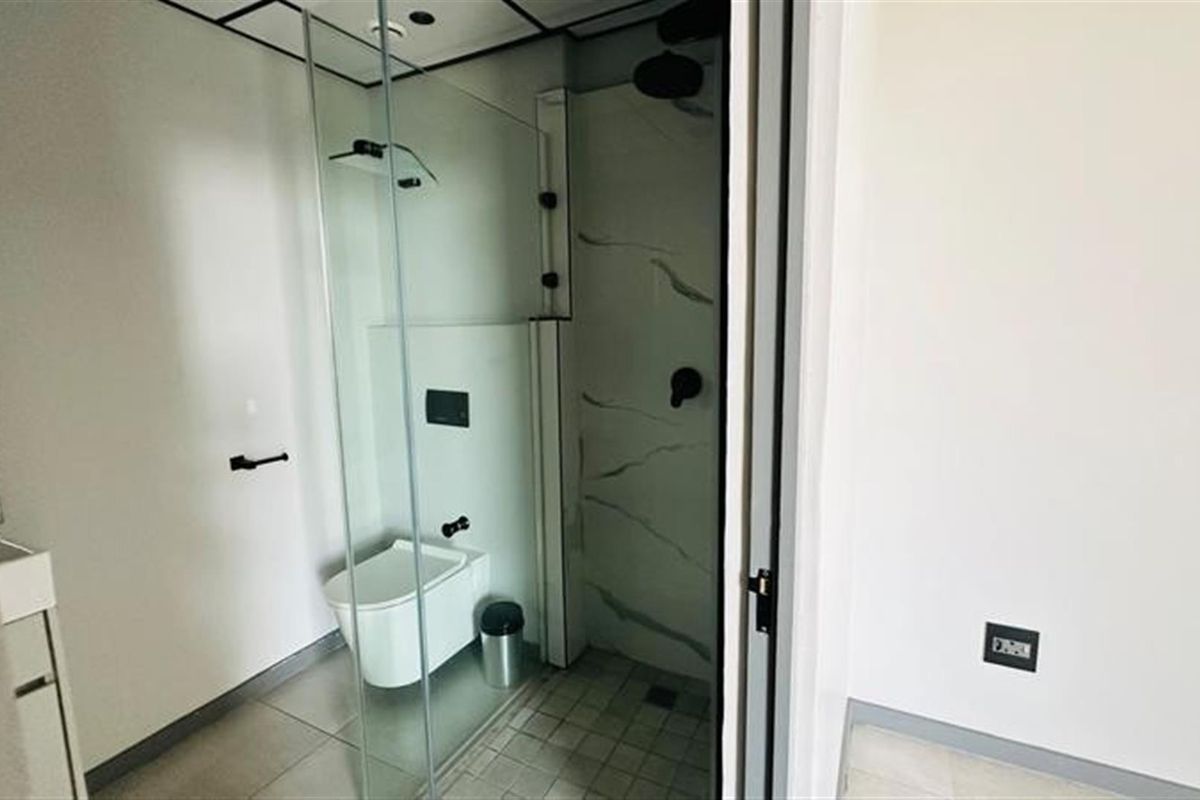 Modern bathroom featuring a glass-enclosed walk-in shower with marble-look tiling, wall-mounted toilet, and contemporary black fixtures.