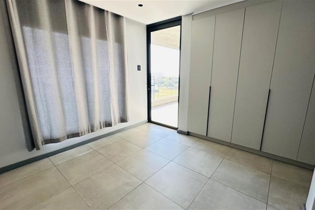 A bright, modern bedroom featuring neutral floor tiles, built-in floor-to-ceiling cabinetry, and direct access to an outdoor balcony.
