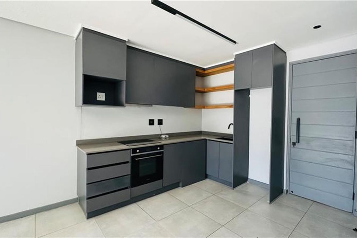 Modern kitchen featuring sleek dark grey cabinetry, integrated oven and hob, stone countertops, and open timber shelving, adjacent to the main entrance door.