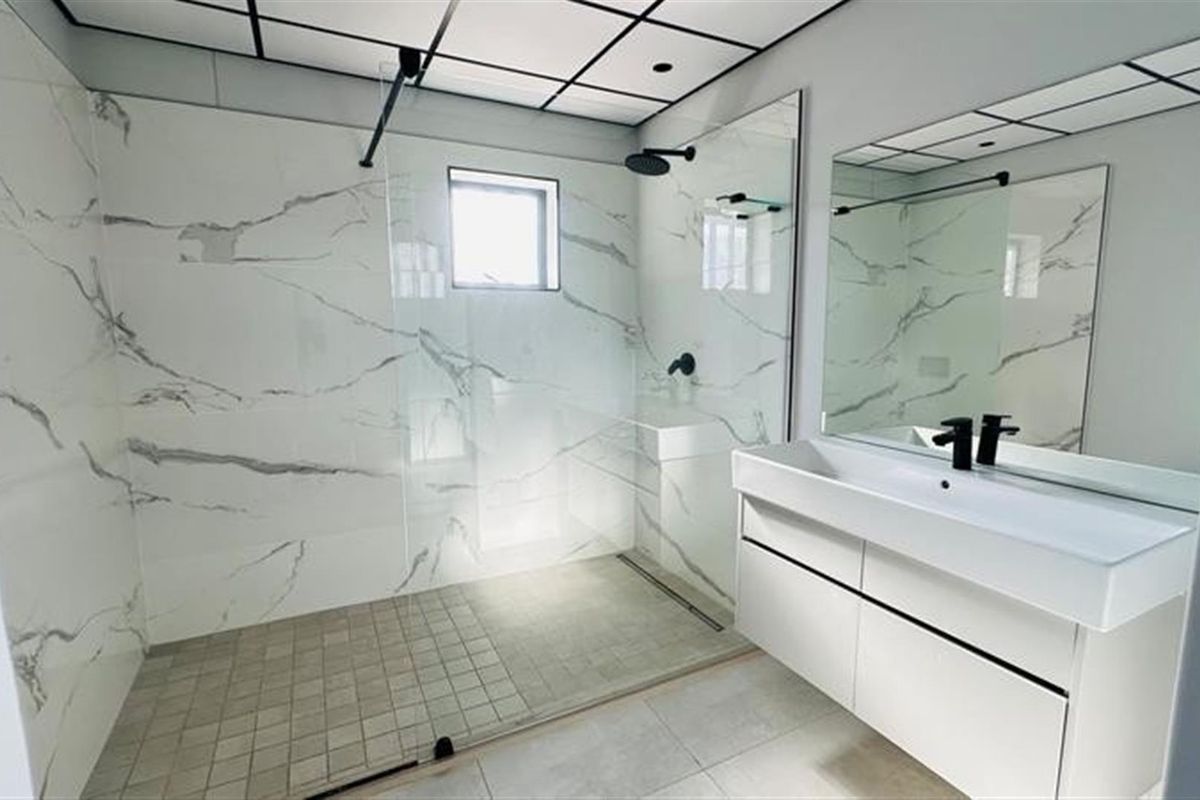 Modern bathroom featuring a spacious walk-in shower with marble-look wall tiles, a sleek vanity with black fixtures, and a contemporary grid-pattern ceiling.
