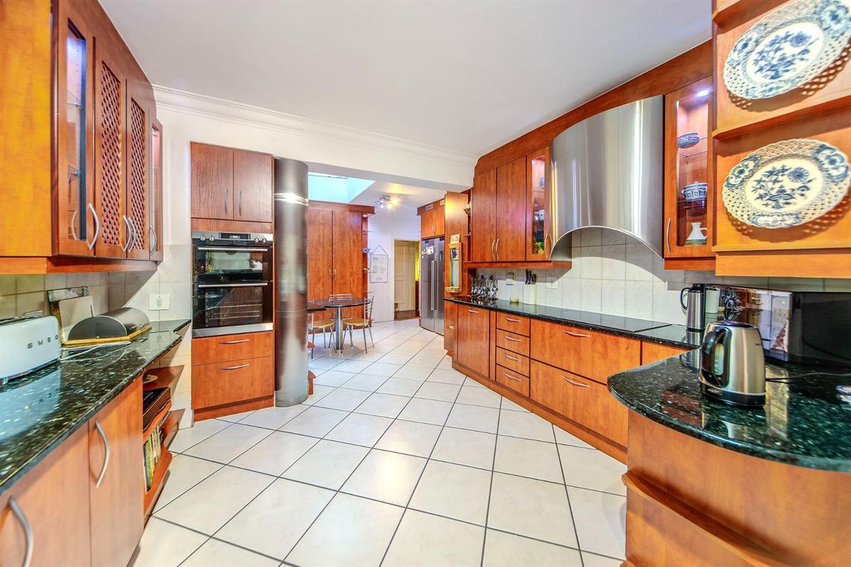 A spacious kitchen featuring warm-toned wooden cabinetry, dark granite countertops, a built-in oven, and a stainless steel extractor fan with tiled flooring.