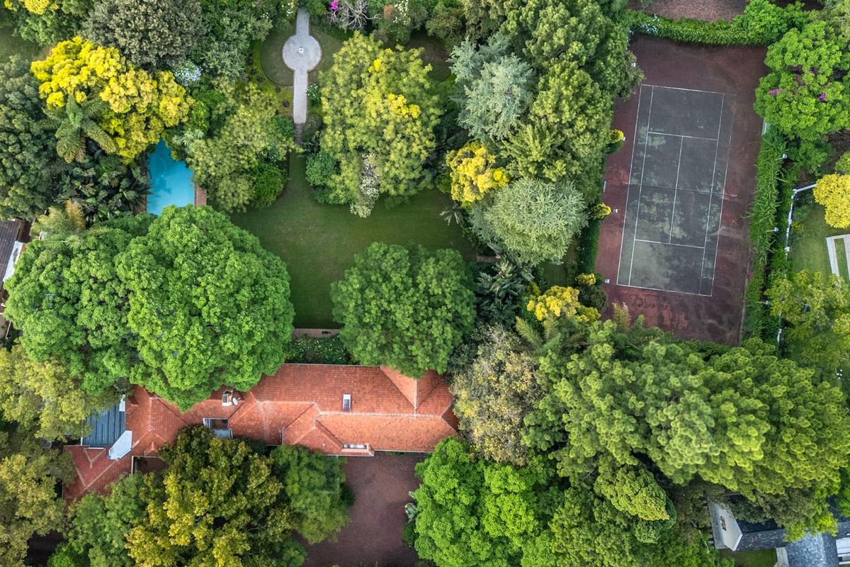 Aerial view of a large residential property featuring a lush garden, swimming pool, and a private tennis court.