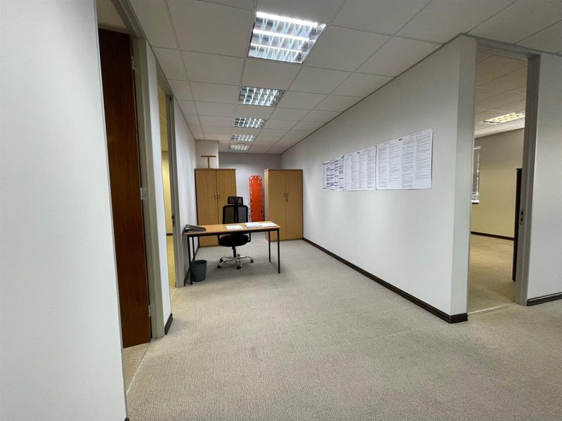 A functional office space featuring carpeted flooring, suspended ceilings with recessed lighting, and built-in storage cupboards.