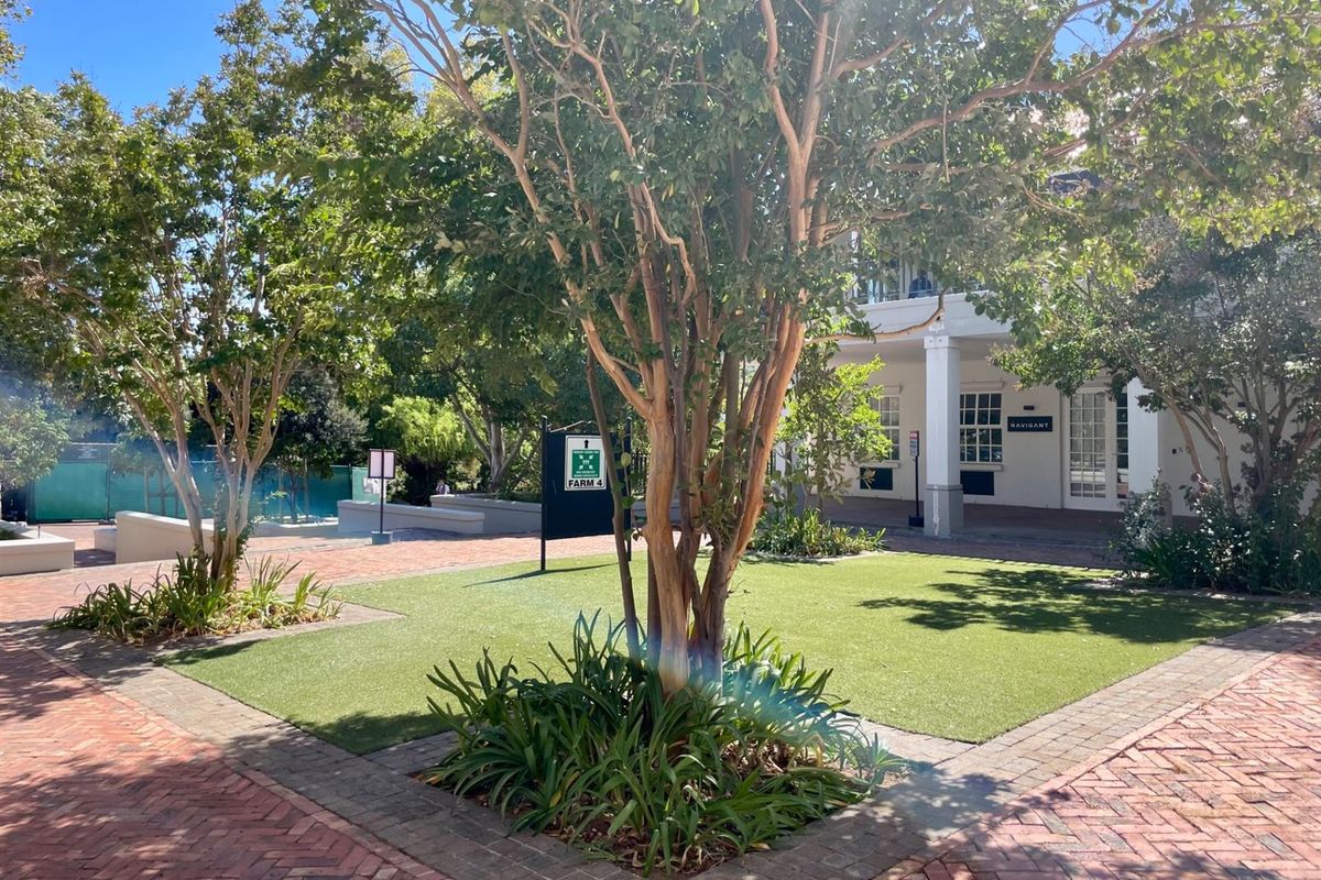 A well-maintained outdoor courtyard area featuring brick paving, artificial lawn, mature trees, and a covered patio entrance to the office building.