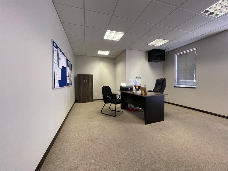 A functional office space featuring neutral carpeting, a suspended ceiling with recessed lighting, and window blinds, providing a professional work environment.