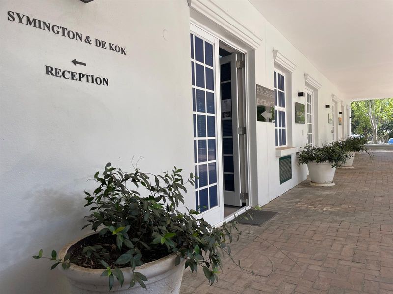 A well-maintained office entrance featuring a covered brick-paved walkway, white facade, and clear directional signage for visitors.