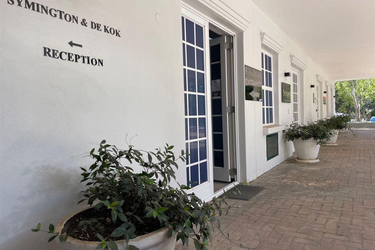 A well-maintained office entrance featuring a covered brick-paved walkway, white facade, and clear directional signage for visitors.